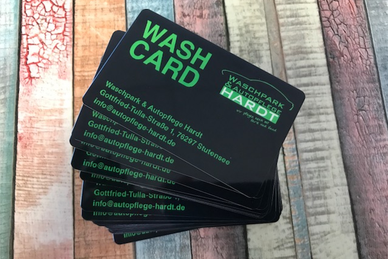 Stapel von schwarzen "Wash Card"-Karten mit grüner Schrift für "Waschpark & Autopflege Hardt" auf einem bunt gestreiften Holztisch.