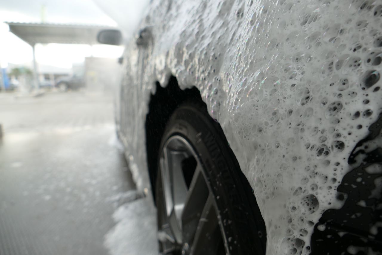 Ein Auto wird mit Schaumseife gewaschen, der Reifen und die Felge sind im Vordergrund sichtbar.