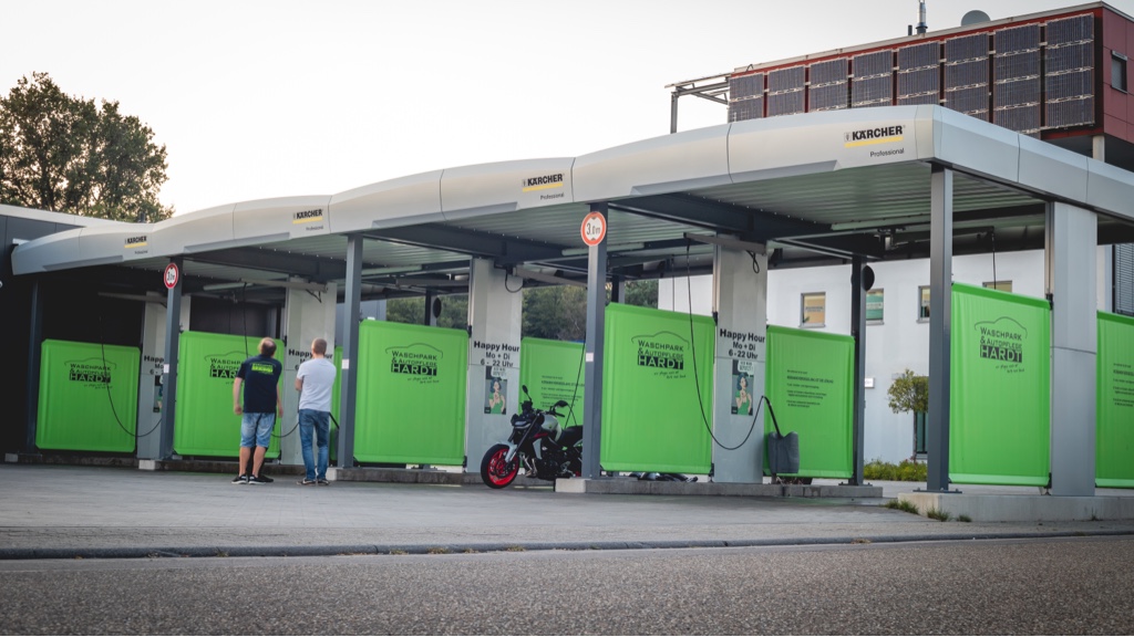 Zwei Personen stehen vor einer Kärcher-Waschanlage mit grünen Abtrennungen und Solarpanelen auf dem Dach.