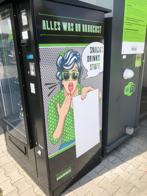 Automat mit Aufschrift "Alles was du brauchst: Snacks, Drinks, Stuff" und Cartoon-Illustration einer Frau mit grünen Sonnenbrillen und Polka-Dot-Shirt.